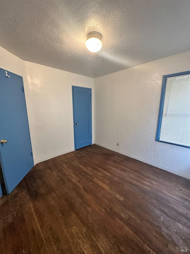 spare room featuring a textured ceiling and dark wood-type flooring