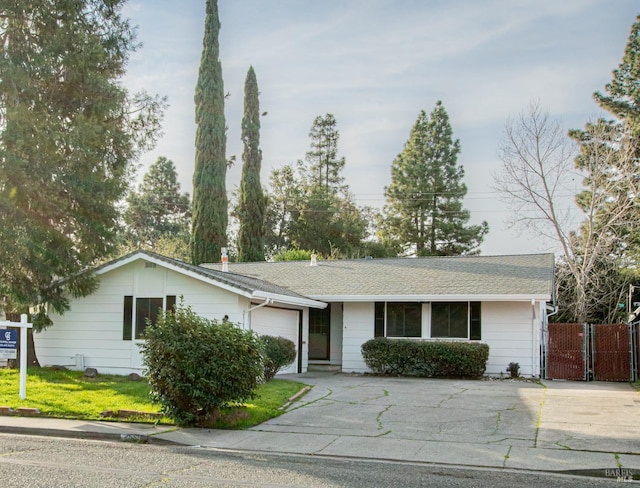 single story home featuring a shingled roof, concrete driveway, a gate, a garage, and a front lawn