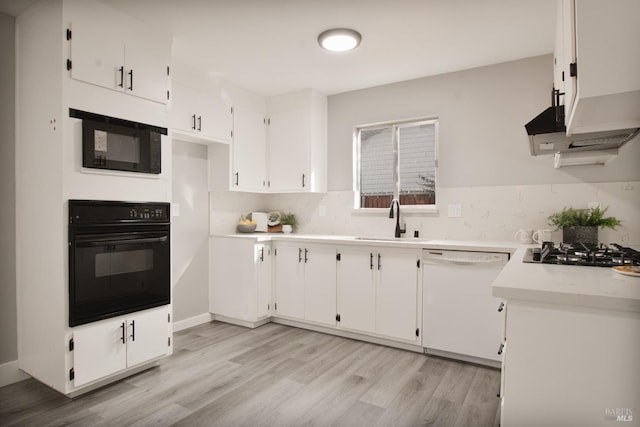 kitchen with white cabinets, light wood-style floors, light countertops, black appliances, and a sink