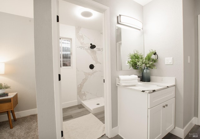 bathroom with baseboards, vanity, and a marble finish shower