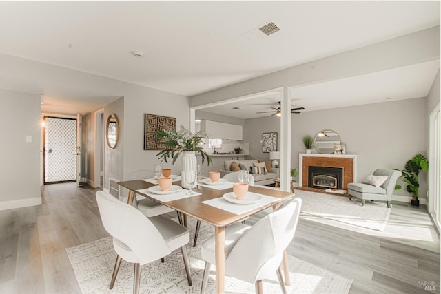 dining area featuring light wood-style floors, ceiling fan, a fireplace, and baseboards