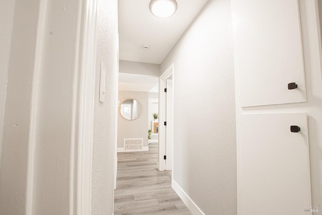 corridor with light wood-style flooring, visible vents, and baseboards