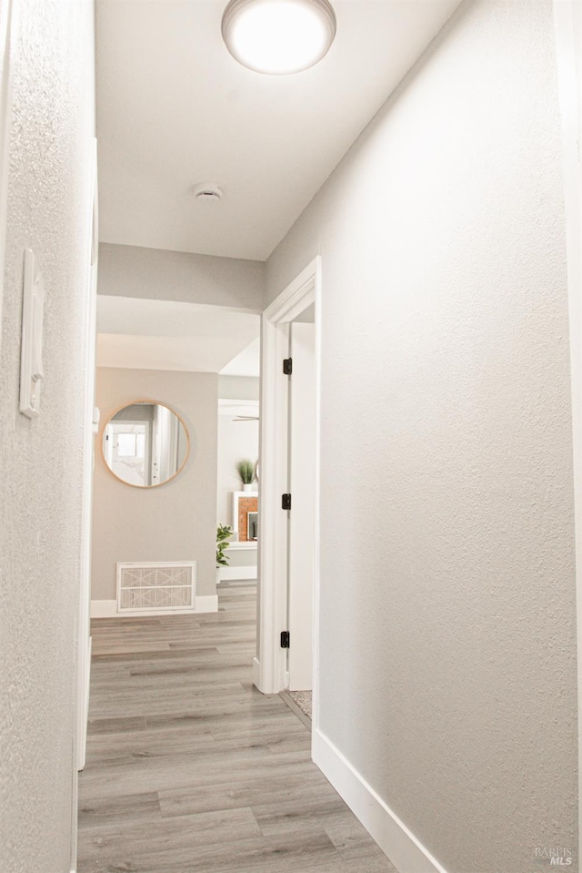 hallway with light wood finished floors, baseboards, and visible vents