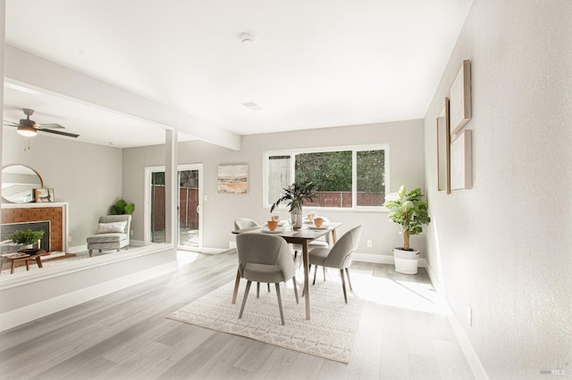 dining room with baseboards, ceiling fan, light wood-style floors, a fireplace, and beam ceiling