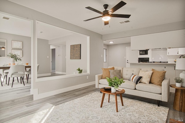 living area featuring light wood-style floors, baseboards, visible vents, and a ceiling fan