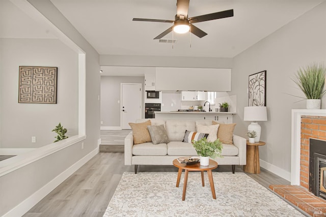 living room with light wood-style flooring, a brick fireplace, visible vents, and baseboards