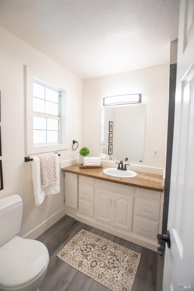 bathroom with toilet, baseboards, wood finished floors, and vanity