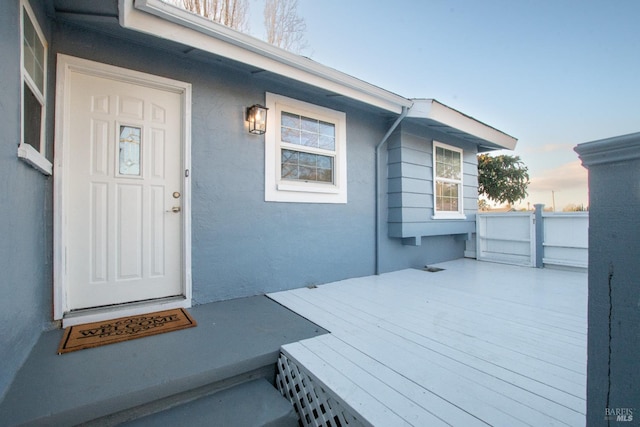 exterior entry at dusk featuring a wooden deck and stucco siding