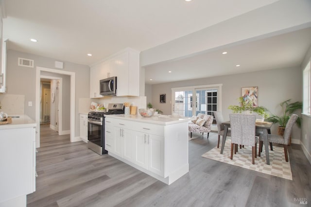 kitchen with a peninsula, visible vents, white cabinetry, light countertops, and appliances with stainless steel finishes