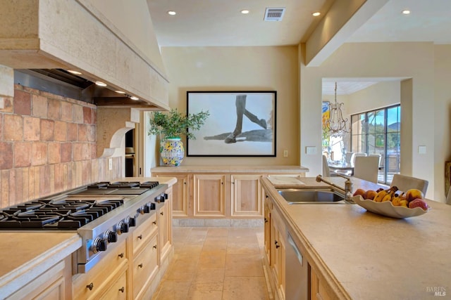 kitchen featuring backsplash, premium range hood, stainless steel appliances, sink, and a notable chandelier