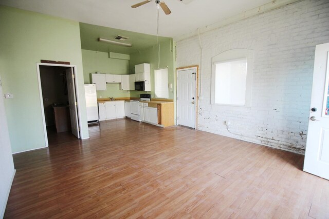 unfurnished living room with ceiling fan, a towering ceiling, brick wall, and light hardwood / wood-style flooring