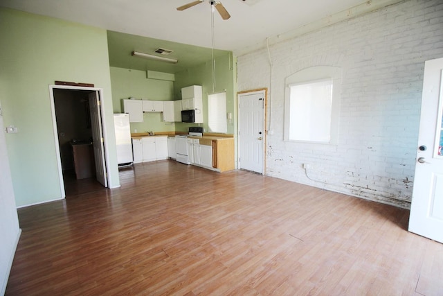 interior space featuring a towering ceiling, brick wall, ceiling fan, and wood finished floors