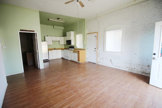 unfurnished living room with visible vents, ceiling fan, wood finished floors, and brick wall