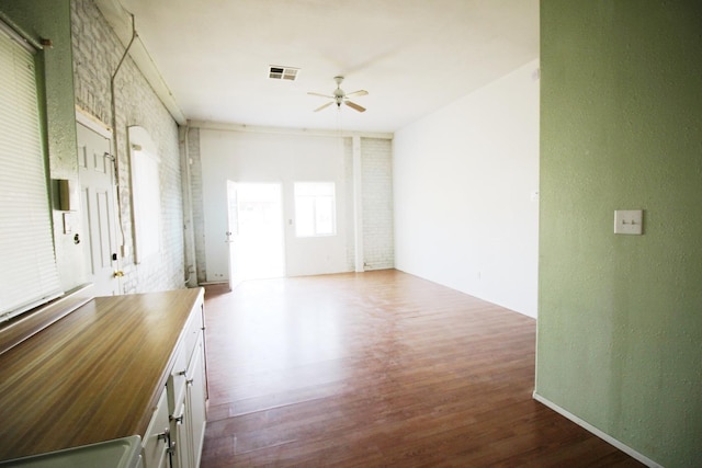 unfurnished room featuring visible vents, wood finished floors, ceiling fan, and brick wall