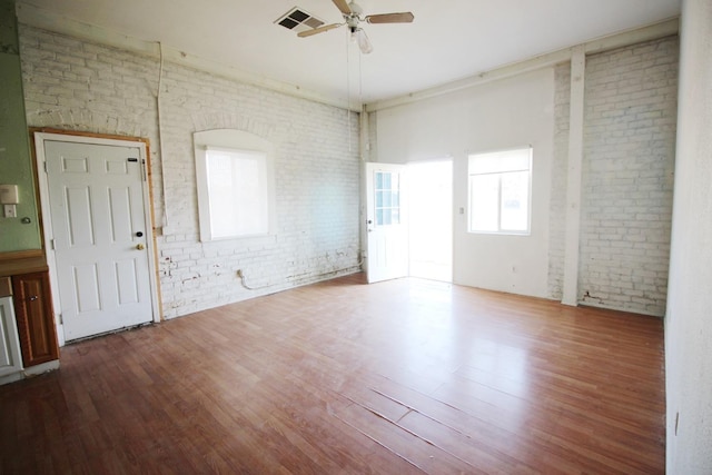 empty room with wood finished floors, visible vents, brick wall, and ceiling fan