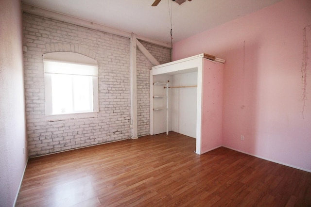 unfurnished bedroom with a ceiling fan, wood finished floors, and brick wall