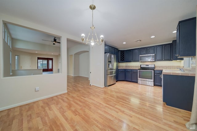 kitchen featuring blue cabinetry, appliances with stainless steel finishes, decorative light fixtures, tile countertops, and light wood-type flooring