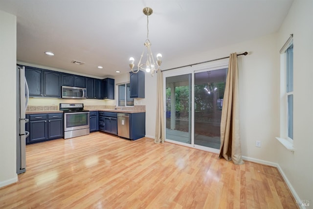 kitchen with blue cabinetry, an inviting chandelier, hanging light fixtures, appliances with stainless steel finishes, and light hardwood / wood-style floors