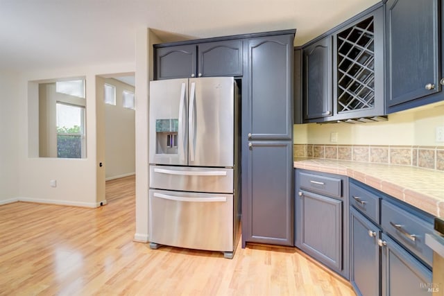 kitchen with blue cabinets, tile counters, light hardwood / wood-style floors, and stainless steel refrigerator with ice dispenser