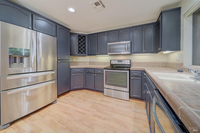 kitchen with sink, tile counters, light hardwood / wood-style floors, and appliances with stainless steel finishes