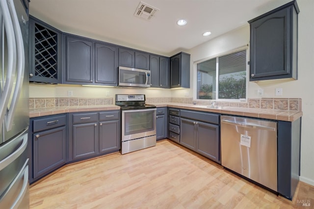 kitchen with stainless steel appliances, tile countertops, sink, and light wood-type flooring