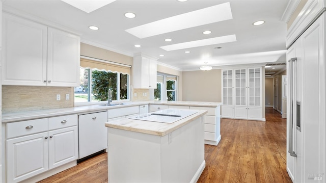 kitchen with a skylight, a kitchen island, tasteful backsplash, light hardwood / wood-style floors, and white cabinetry