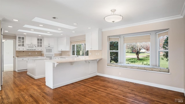 kitchen featuring a skylight, dark wood-type flooring, kitchen peninsula, white appliances, and white cabinets