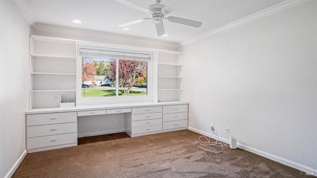 unfurnished office with built in desk, dark carpet, ceiling fan, and crown molding