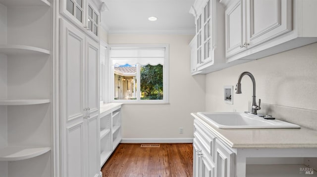 interior space with white cabinetry, dark hardwood / wood-style flooring, ornamental molding, and sink