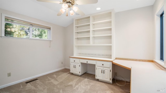 unfurnished office featuring built in desk, light colored carpet, and ceiling fan