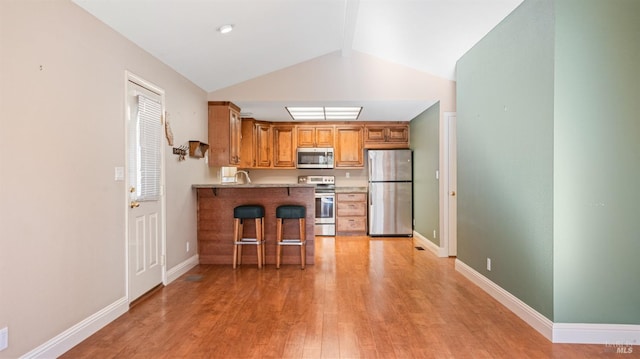 kitchen featuring light hardwood / wood-style flooring, vaulted ceiling, a kitchen bar, kitchen peninsula, and stainless steel appliances