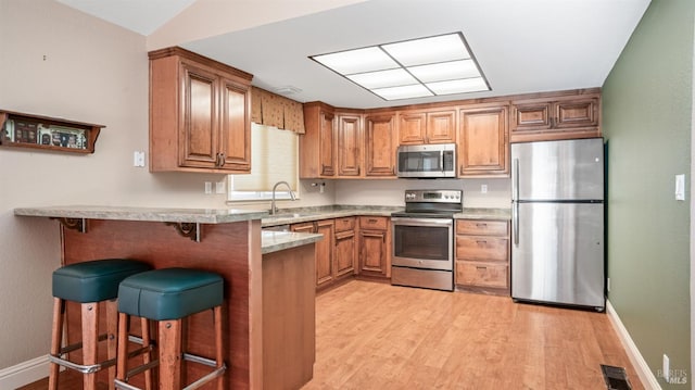 kitchen featuring a breakfast bar, stainless steel appliances, vaulted ceiling, sink, and light hardwood / wood-style floors