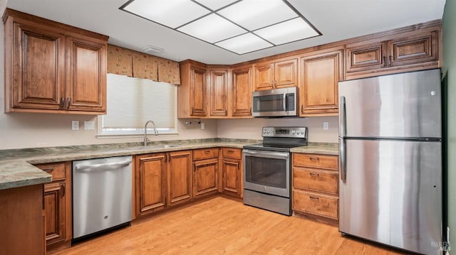 kitchen with light stone countertops, sink, light wood-type flooring, and appliances with stainless steel finishes