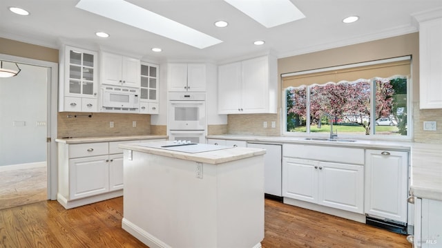 kitchen with a skylight, sink, a center island, white cabinets, and light wood-type flooring