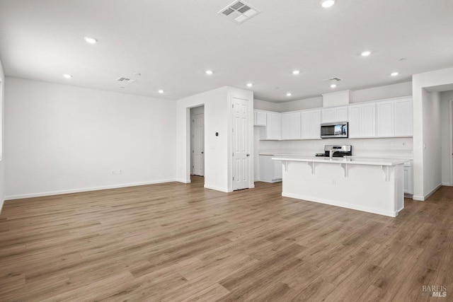 kitchen with white cabinets, a center island with sink, stainless steel appliances, and a breakfast bar area