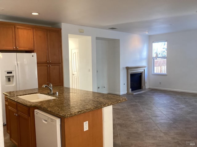 kitchen with a kitchen island with sink, sink, white appliances, dark tile patterned flooring, and dark stone countertops