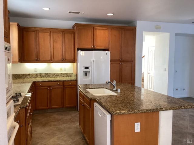 kitchen featuring white appliances, sink, dark stone counters, tile patterned flooring, and a kitchen island with sink