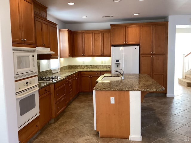 kitchen with white appliances, dark stone countertops, a center island with sink, sink, and a breakfast bar area