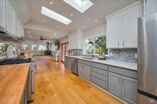 kitchen with wooden counters, appliances with stainless steel finishes, vaulted ceiling with skylight, sink, and white cabinetry