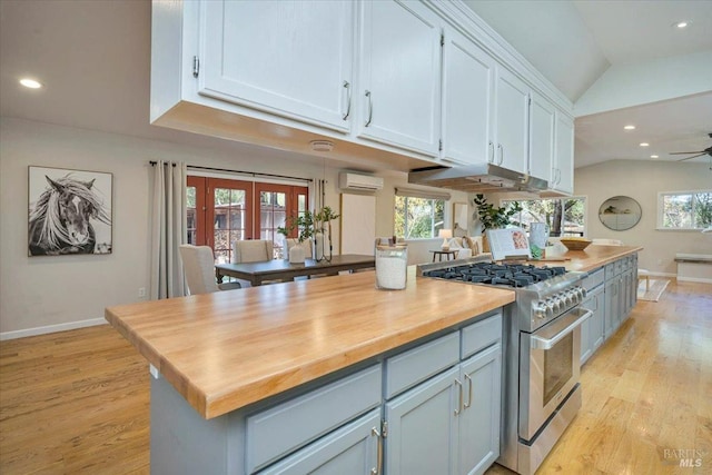 kitchen with a wall mounted air conditioner, wood counters, lofted ceiling, and high end stainless steel range