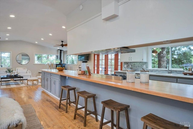 kitchen featuring white cabinetry, ceiling fan, a kitchen breakfast bar, light hardwood / wood-style flooring, and lofted ceiling