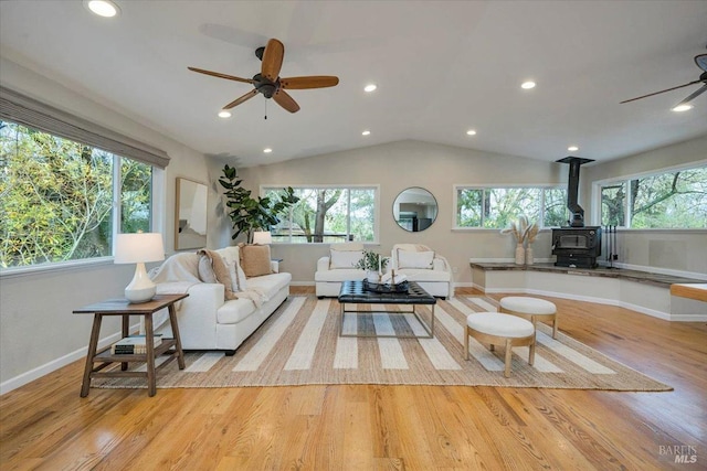 living room featuring plenty of natural light, light hardwood / wood-style floors, a wood stove, and vaulted ceiling