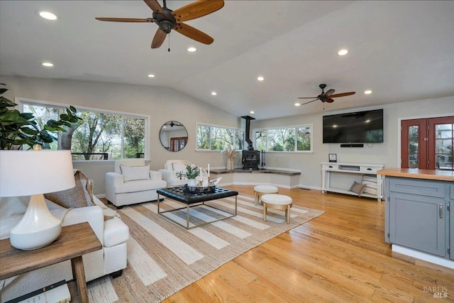 living room featuring vaulted ceiling, light hardwood / wood-style flooring, a wood stove, and plenty of natural light