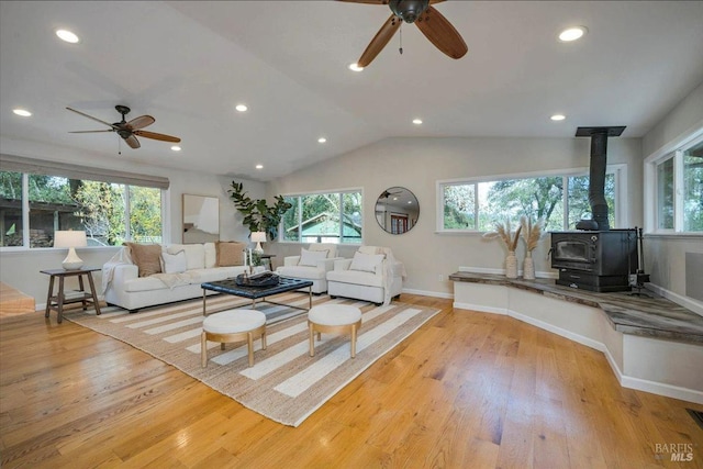 living room with vaulted ceiling, light hardwood / wood-style flooring, a wood stove, and ceiling fan