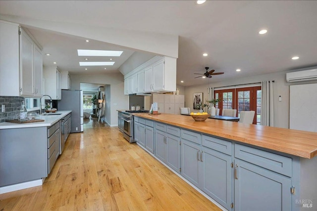 kitchen featuring wooden counters, white cabinets, ceiling fan, light hardwood / wood-style floors, and stainless steel appliances