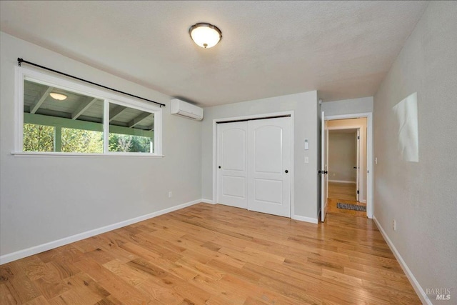 unfurnished bedroom with a textured ceiling, a closet, a wall mounted air conditioner, and light wood-type flooring