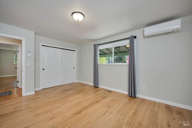 unfurnished bedroom with light hardwood / wood-style floors, an AC wall unit, and a closet