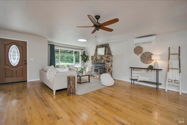 living room with a wood stove, ceiling fan, an AC wall unit, lofted ceiling, and light wood-type flooring