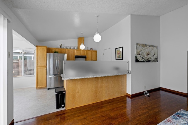 kitchen featuring light countertops, freestanding refrigerator, under cabinet range hood, vaulted ceiling, and pendant lighting
