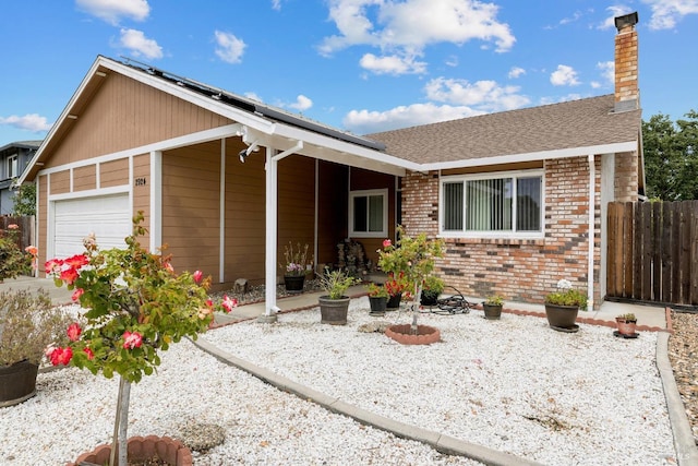ranch-style home featuring fence, brick siding, a garage, a chimney, and solar panels